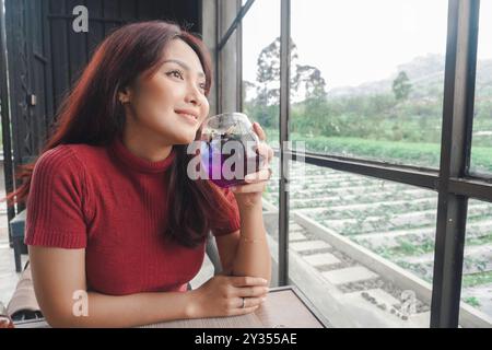 Ritratto di una giovane donna gioiosa che beve una tazza di tè a casa. Bella ragazza sorridente che beve tè telang nella stagione delle piogge. Foto Stock