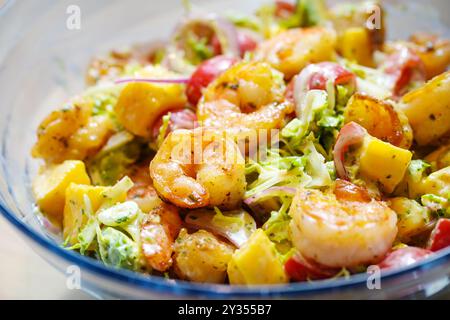 Insalata di pesce con gamberetti, mango, avocado, lattuga e pomodori con condimento alle erbe in una ciotola di vetro, piatto fresco per feste, shot ravvicinato, spazio copia, sele Foto Stock