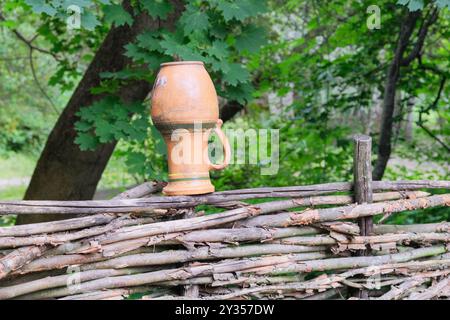 Vaso di ceramica su una recinzione di vimini in campagna. Arte etnica. Foto Stock