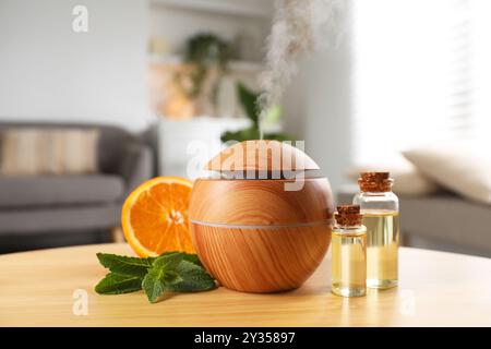 Diffusore di olio essenziale, prodotti cosmetici, menta e arancia su tavola di legno a casa Foto Stock