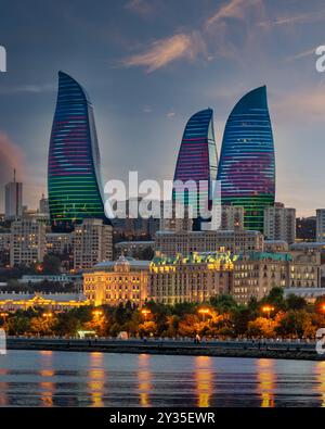 Le Torri della fiamma si ergono alte contro il cielo serale, illuminate dalla colorata bandiera dell'Azerbaigian e riflettono sull'acqua. Il vivace display mette in risalto le moderne realizzazioni architettoniche di Baku Foto Stock