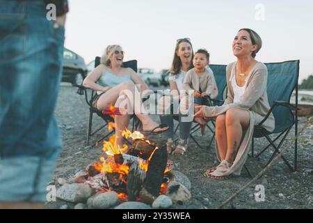 Un gruppo di amici seduti intorno a un falò sulla spiaggia al tramonto. Foto Stock