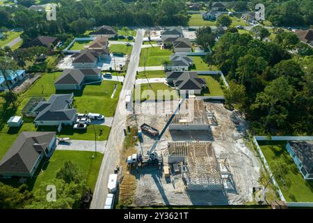 Costruttori professionali e gru camion che lavorano sulla costruzione di tetti di casa suburbana non finita con struttura a telaio in legno nella zona rurale della Florida. Conc Foto Stock