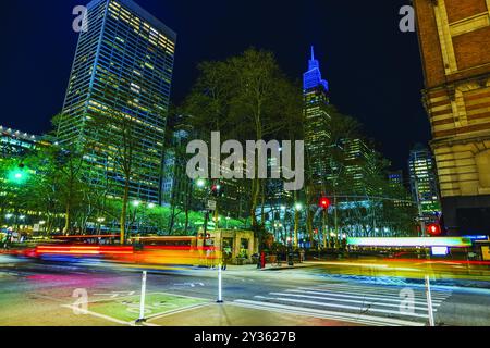 Vista notturna di una strada trafficata della città con sentieri leggeri dalle auto contro grattacieli e alberi sotto le luci urbane. Nuovo Yor. STATI UNITI. Foto Stock