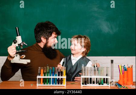 Insegnante che aiuta il ragazzo con la lezione. Allegro ragazzo sorridente e insegnante che si diverte contro la parete blu. Genitorialità. Ritorno a scuola. Foto Stock