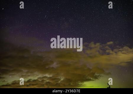 Un cielo notturno pieno di stelle, parzialmente oscurato dalle nuvole. La scena presenta una sfumatura di colori che va dal blu scuro al verde, suggerendo atmos Foto Stock