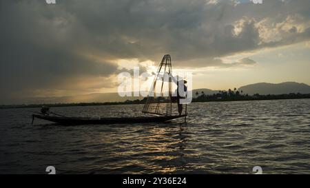 Fisherman Balancing on Boat presso il lago Inle, Myanmar al tramonto Foto Stock