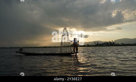 Fisherman Balancing on Boat presso il lago Inle, Myanmar al tramonto Foto Stock