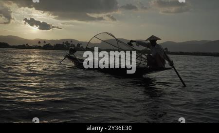 Fisherman Balancing on Boat presso il lago Inle, Myanmar al tramonto Foto Stock