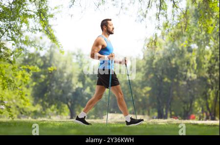 Foto a tutta lunghezza di un uomo che cammina con pali da trekking in un parco Foto Stock