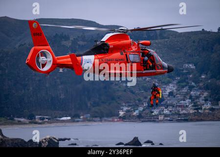 Un meccanico di volo a bordo di un elicottero MH-65 Dolphin della Guardia Costiera di San Francisco abbassa il nuotatore di soccorso fino a una scogliera vicina mentre pugnala Foto Stock