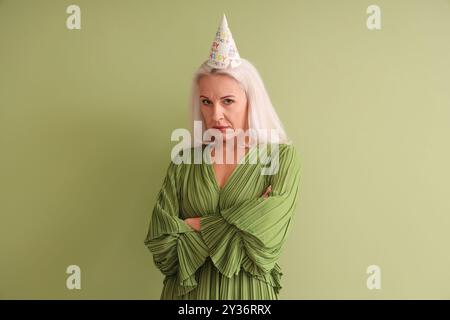 Sconvolta una donna matura con un cappello da festa su sfondo verde Foto Stock