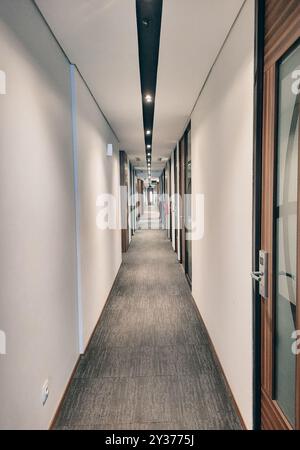 Corridoio di uffici vuoto e stretto con luce calda e interni di ufficio. Foto Stock