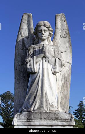 Statua di un angelo che prega su uno sfondo blu del cielo Foto Stock