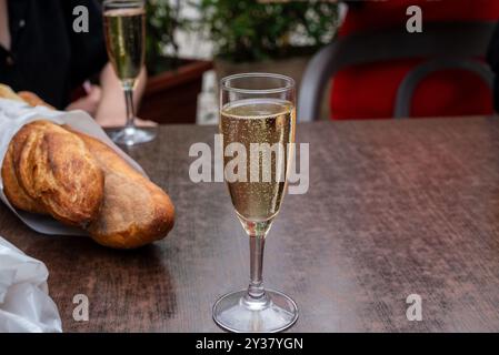 bicchiere di vino bianco frizzante su un tavolo con baguette francese sullo sfondo Foto Stock