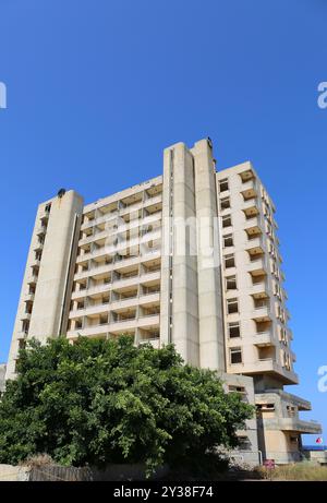 VAROSHA, FAMAGOSTA, CIPRO NORD - 30 AGOSTO 2023: Hotel abbandonato con sfondo Blue Sky e Tree by the Beach Foto Stock