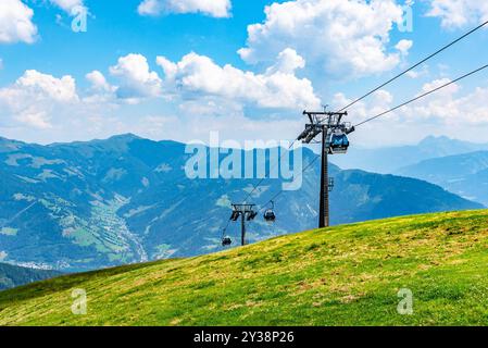 I visitatori fanno un giro in funivia a Schmittenhohe, ammirando viste mozzafiato delle Alpi austriache in una giornata di sole. I lussureggianti pendii verdi contrastano splendidamente con il cielo blu e le montagne lontane. Foto Stock