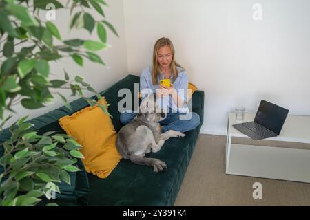 giovane donna con un cane che usa lo smartphone sul divano di casa Foto Stock