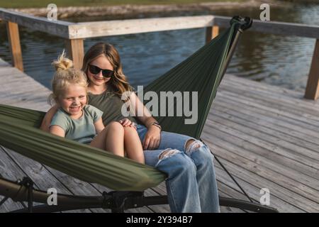 Due ragazze sedute sull'amaca al lago ridendo insieme Foto Stock