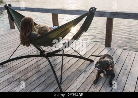 Persone che si rilassano nell'amaca sul lago con cani nelle vicinanze Foto Stock