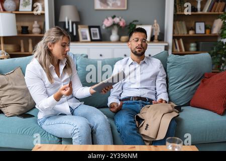 Concetto di shopping. Una giovane coppia d'affari seduto a casa sul divano discutendo della donna che spende i soldi, acquista e ordina online con il marito Foto Stock