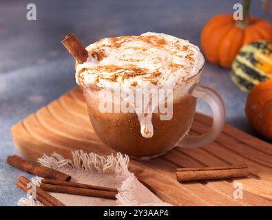 Latte di zucca ghiacciata con panna montata e cannella traboccante da una tazza di vetro Foto Stock