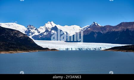 Vista panoramica dello splendido ghiacciaio Perito Moreno, circondato da maestose cime di montagna sotto un cielo azzurro. Foto Stock