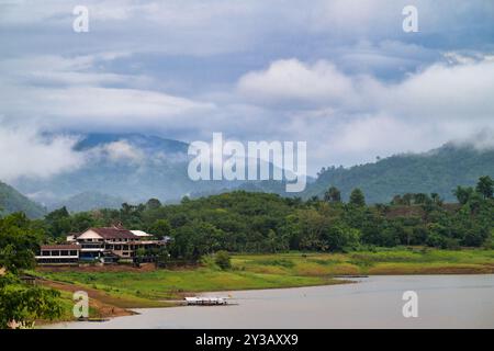 Sangkhla Buri, provincia di Kanchanaburi, Un tranquillo villaggio annidato tra lussureggianti montagne verdi e un tranquillo lago, con nebbia che si diffonde da lontano Foto Stock