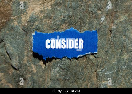 Considerare il messaggio scritto su un pezzo di carta blu strappato con sfondo in pietra. Simbolo concettuale da considerare. Copia spazio. Foto Stock