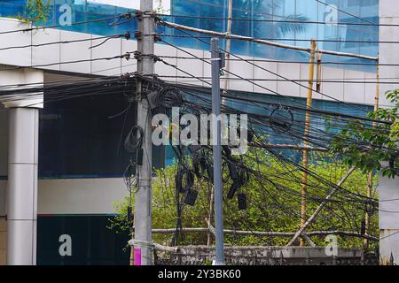 Pali elettrici con fili disordinati, cavi elettrici impigliati e di telecomunicazione sui pali sul lato di una strada cittadina Foto Stock