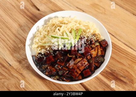 Jajangmyeon o Jjajangmyeon, tagliatelle coreane con salsa nera su piatto bianco, condimento con semi di sesamo arrosto e cetriolo Kyuri Foto Stock