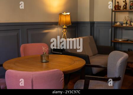 Accogliente soggiorno con tavolo in legno e sedie color pastello durante un tranquillo pomeriggio Foto Stock