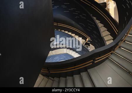 Donna su scala a chiocciola stampata con parole finlandesi, Biblioteca centrale e Centro culturale Oodi, progetto di ala Architects, Helsinki, Finlandia, Europa Foto Stock