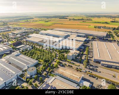 Area industriale con diversi grandi edifici, circondata da campi verdi e alberi, un cielo luminoso e spazioso sopra, area industriale Wolfsberg, Nagold Foto Stock