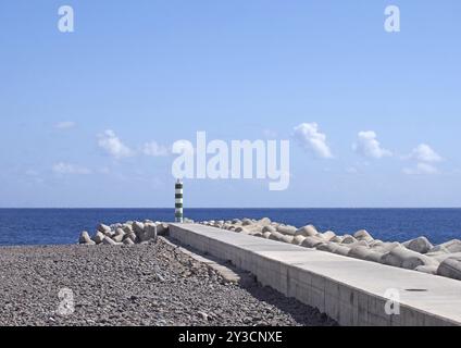 Un molo e un frangiflutti con faro sulla spiaggia di funchal madeira, con un mare e un cielo luminosi e soleggiati Foto Stock