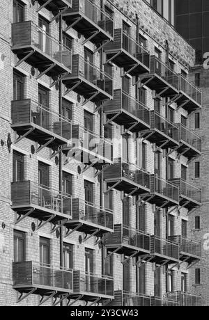 Una vista prospettica monocromatica della facciata di un grande edificio vecchio mulino in pietra convertito in appartamenti con moderni balconi in vetro Foto Stock