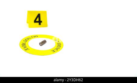 Un involucro di proiettile esaurito collocato all'interno di un cerchio giallo, etichettato con il testo "Evidence, do not move" (prova, non spostare), con un tag con numero 4 sfocato, posto contro una b bianca Foto Stock