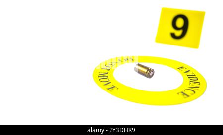 Un involucro di proiettile esaurito collocato all'interno di un cerchio giallo, etichettato con il testo "Evidence, do not move" (prova, non spostare), con un tag con numero 9 sfocato, posto contro una b bianca Foto Stock