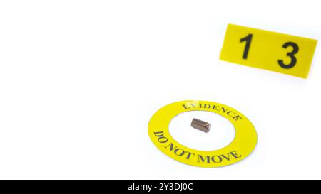 Involucro di un proiettile esaurito collocato all'interno di un cerchio giallo, etichettato con il testo "Evidence, do not move" (prova, non spostare), con un'etichetta sfocata con il numero 1, posta contro una b bianca Foto Stock