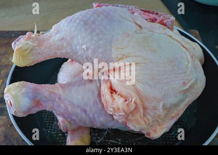 Un pollo intero crudo e crudo su una padella nera in un ambiente di cucina. Foto Stock