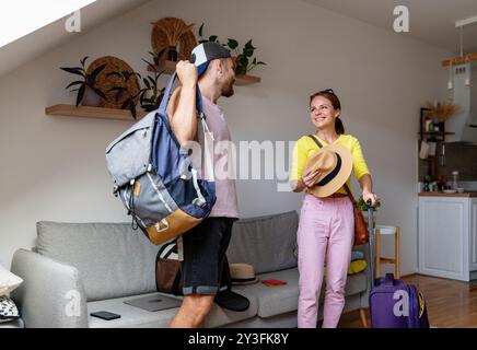 Giovane vera coppia sposata con borse da viaggio in piedi nel loro appartamento, pronta a partire per il loro viaggio. Foto Stock