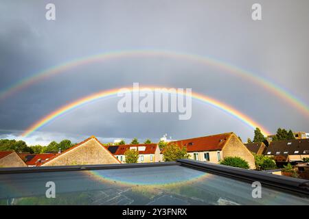 Luminoso e colorato doppio arcobaleno sopra un'area residenziale nei Paesi Bassi. Parte dell'arcobaleno si riflette in un lucernario. Foto Stock
