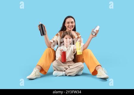 La bambina e sua madre con le lattine di vernice spray sedute su sfondo blu Foto Stock