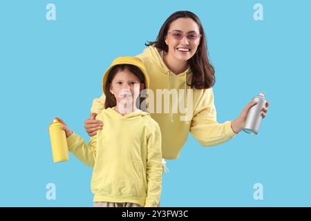 La bambina e sua madre con bombolette spray su sfondo blu Foto Stock