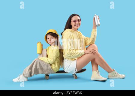 La bambina e sua madre con le lattine di vernice spray sedute sullo skateboard su sfondo blu Foto Stock