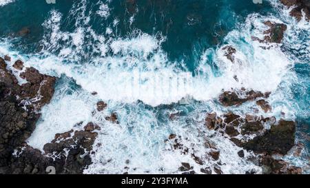 Vista aerea delle onde oceaniche che si infrangono contro le aspre rocce costiere, che mostrano la bellezza dinamica della turbolenta schiuma marina e della costa rocciosa. Foto Stock
