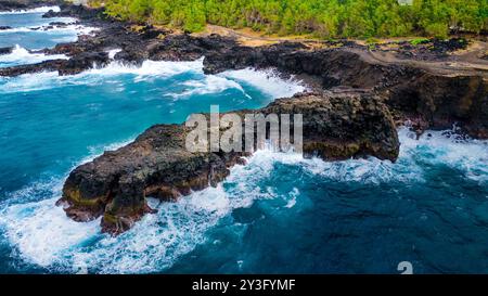 Immagine aerea di spettacolari scogliere rocciose che si prosciugano nel mare con onde che si infrangono contro la loro base, adagiate su uno sfondo verde lussureggiante. Foto Stock