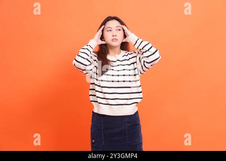 un gesto di donna asiatica sincero e bella soffre di vertigini mal di testa dopo aver fatto i compiti isolato su sfondo arancione Foto Stock