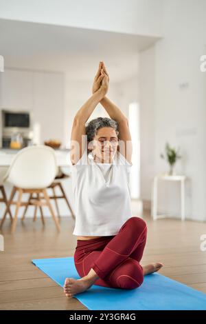 Felice sano in forma donna matura che fa esercizi di yoga seduti a casa. Foto Stock