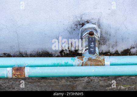 Tubo idraulico e valvola invecchiati sulla parete del tetto di una casa, con un sistema di lavoro dell'acqua posizionato su un vecchio sfondo di cemento. Foto Stock